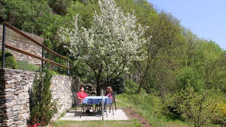 Garden in front of the Bergkirchner vacation apartment, © Bergkirchner Two people are sitting at a table in the garden under a blossoming tree.