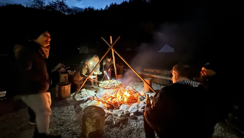 Survival Workshop Wilderness Center Nasswald, © Georg Bergthaler People sitting around an outdoor campfire at night, surrounded by trees.