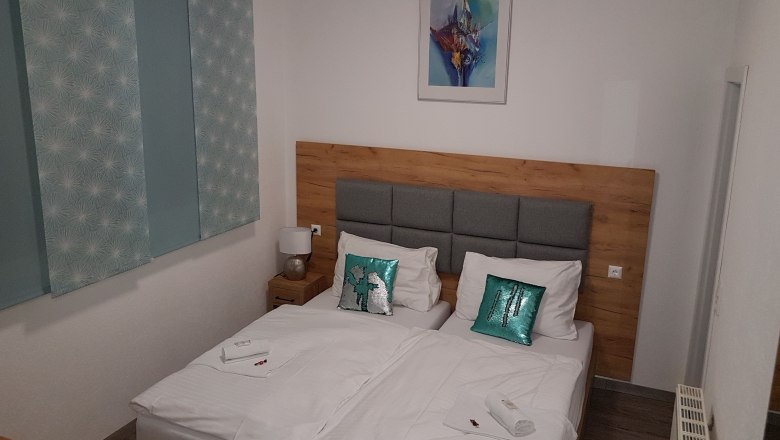 Stay comfortably in a double room, © Konrad Brandl Double room with two single beds, wooden headboard, decorative cushions and a picture on the wall.