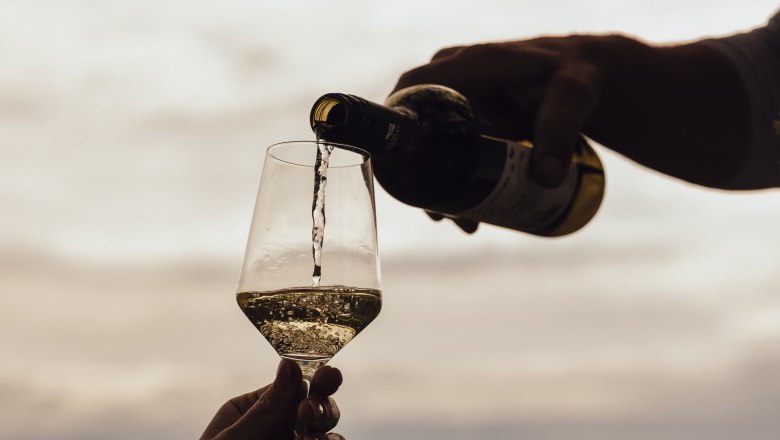 Enjoy the wine, © Weinviertel Tourismus / Sophie Menegaldo Wine is poured into a glass outdoors, with a landscape in the background.