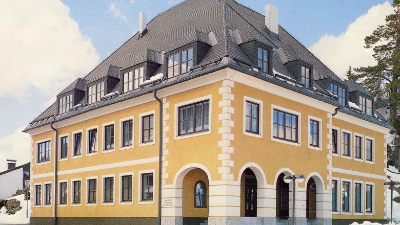 Municipality and tourist office Annaberg, © zVg Gemeinde Annaberg Yellow building with a gray roof and many windows, surrounded by snow.