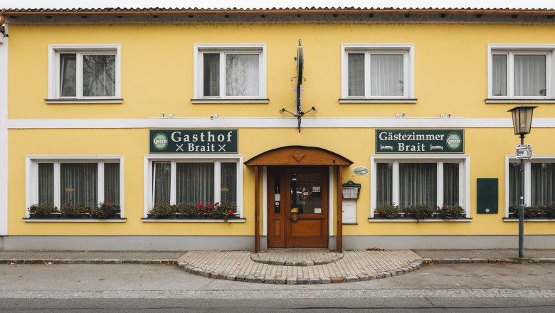 Inn with wine expertise, © Niederösterreich Werbung/David Schreiber Yellow building with signs 'Gasthof Brait' and 'Gästezimmer Brait'.