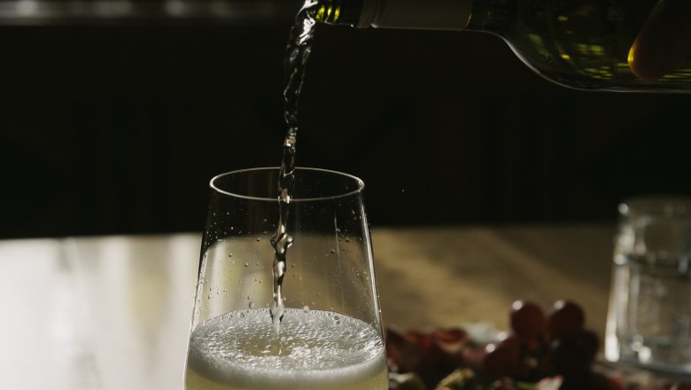 Pouring wine, © Weinviertel Tourismus / Sophie Menegaldo A glass of white wine is poured on a table, with a plate of snacks in the background.