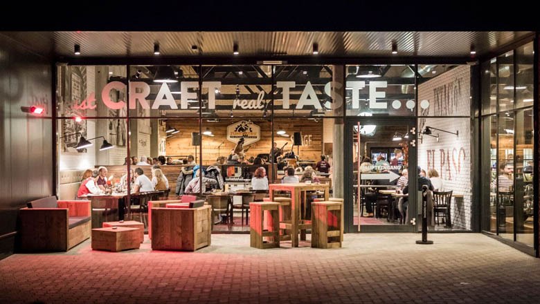 Ignition unit, © Lukas Kirchgasser Photography Exterior view of a restaurant with glass front and wooden furniture.