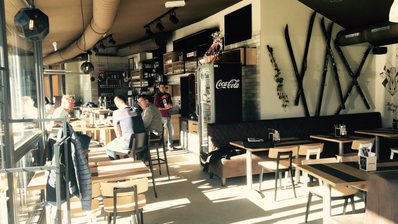 The meeting point for an eventful day in the Wexl Arena, © Familienarena Bucklige Welt-Wechselland GmbH Interior view of a café with wooden furniture and skis on the wall.