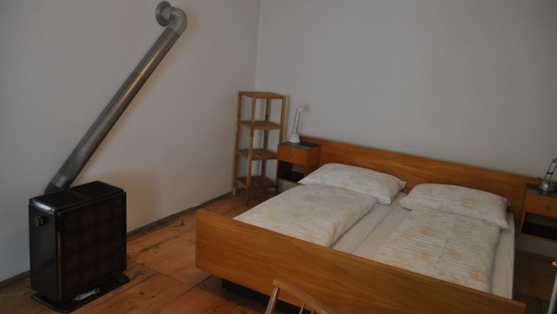 Bedroom, © Familie Ackerl A simply furnished bedroom with double bed, bedside tables, shelf and stove.