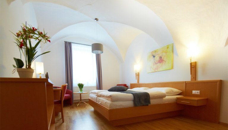 Room 2, © Rathauskeller Melk Bright hotel room with double bed, desk, plants and artwork on the wall.