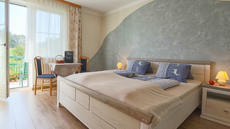 Bedroom at the Mayerhof, © Fam. Mayer Cozy bedroom with double bed, blue bed linen, table with chairs and balcony access. Bright, inviting atmosphere.