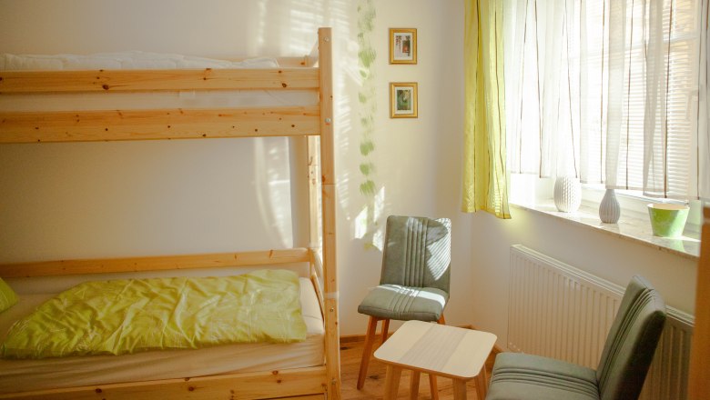 Bunk bed, © Michael Sokolar A bright room with a bunk bed, two chairs, a small table and a window with curtains.