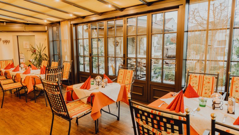Winter and guest garden, © Niederösterreich Werbung/Klaus Engelmayer A cozy winter garden with covered tables and chairs, surrounded by large windows with a view outside.