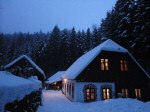 Gillausklause 1, © Stephanus Domanig Snow-covered house in the forest at dusk with illuminated windows.