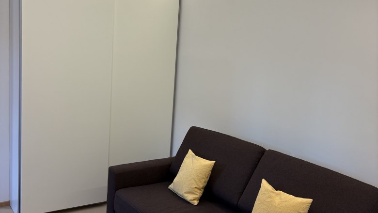 TDR House Morning Sun Living Room, © Fam Pauker Modern living room with brown sofa, yellow cushions and small table with white tablecloth.