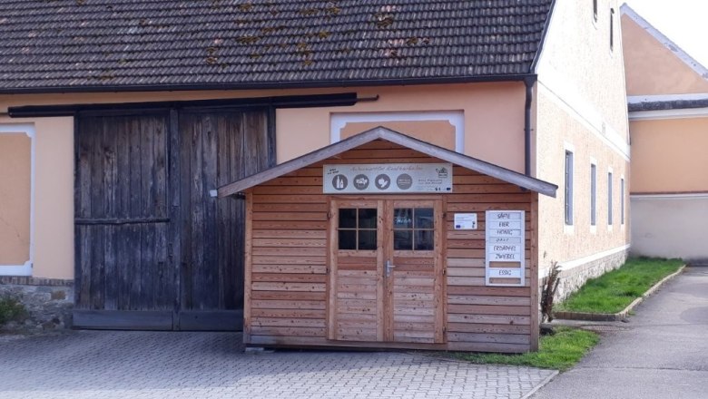 Self-service hut, © Ursula Lembacher A small wooden store in front of a large building with a wooden gate.