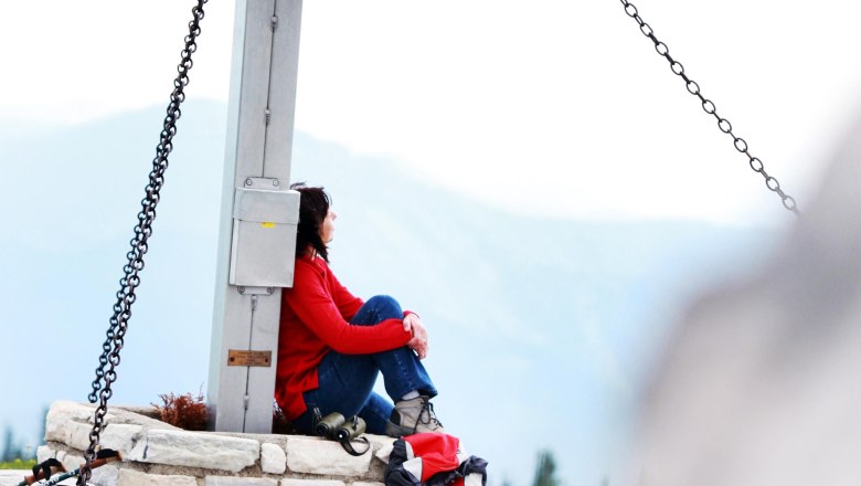 Summit cross on the Tirolerkogel, © weinfranz.at Person sitting at the summit cross of the Tirolerkogel with rucksack.