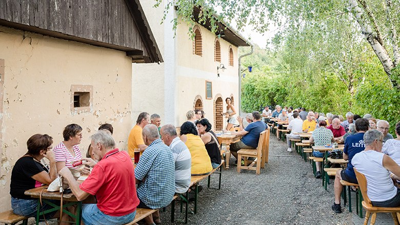 Wine tavern Öfferl, © Weinbau Öfferl People sit at long tables outside at a wine tavern.