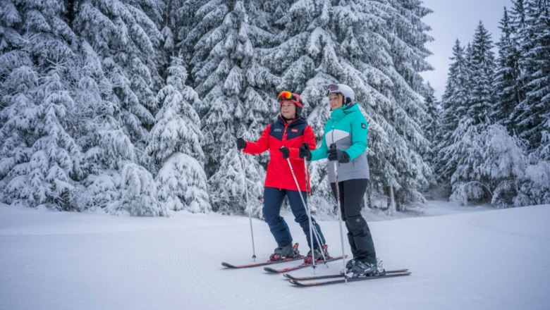 Schidorf Kirchbach, © Waldviertel Tourismus, Robert Herbst Two skiers stand on a snow-covered slope in front of snow-covered trees.