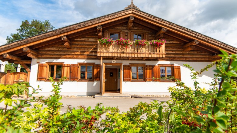 Kaminstubn Schwechat Mannswörth, © Kaminstubn Traditional wooden house with balcony and flower boxes, blue sky in the background.