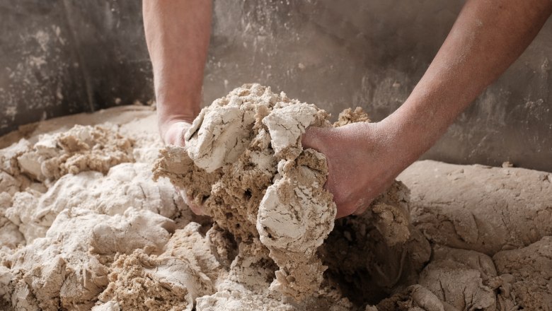 Genuine craftsmanship, © Geier.die Bäckerei Hands knead dough in a large bowl.
