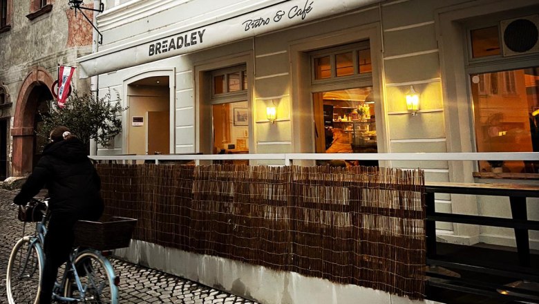 BREADLEY BISTRO, © Marie Grulich Exterior view of a café with a cyclist on cobblestones.