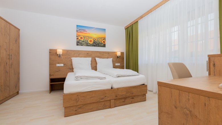 Bedroom, © Schönfelderhof Modern bedroom with wooden furniture, double bed, wardrobe and desk. A picture of sunflowers hangs above the bed.