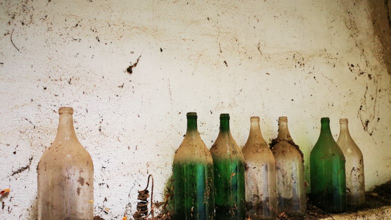 Time seems to stand still here - wine cellar lane Seitweg, © Weinstraße Weinviertel Old, dusty glass bottles on a shelf in a cellar.
