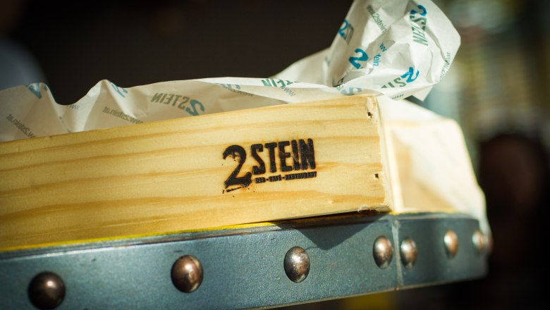2Stein Bar-Café-Restaurant, © 2stein_Kastner new media Wooden box with 2Stein logo and paper in the background.