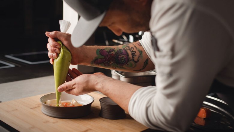 Sustainable great things are being created here, © Niederösterreich Werbung/Daniela Führer A chef decorates a dish with a green sauce from a piping bag.