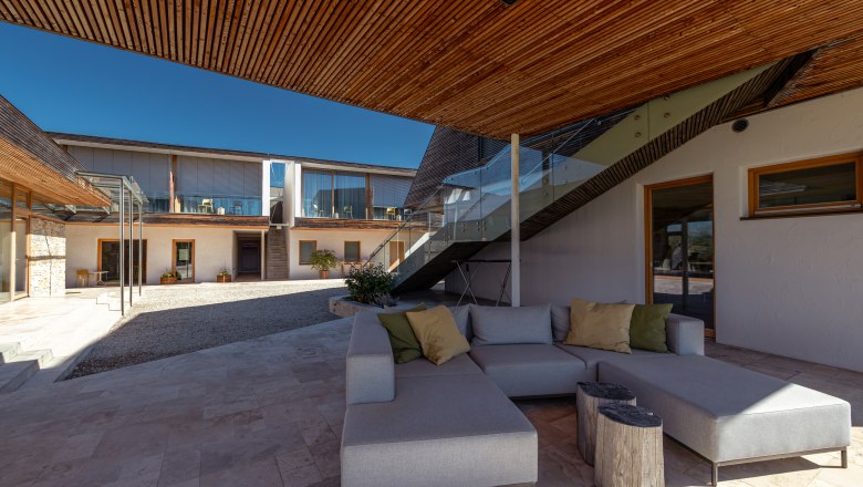 MALAT Winery and Hotel, © Niederösterreich Werbung / Maximilian Pawlikowsky Inner courtyard of a modern building with wooden elements, glass railings and gray seating furniture.