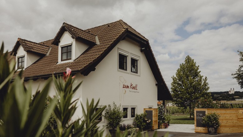 Country inn in Mold in the Horn district, © Niederösterreich Werbung/Sophie Menegaldo A country inn with a brown tiled roof and white façade, surrounded by plants and a wooden fence.