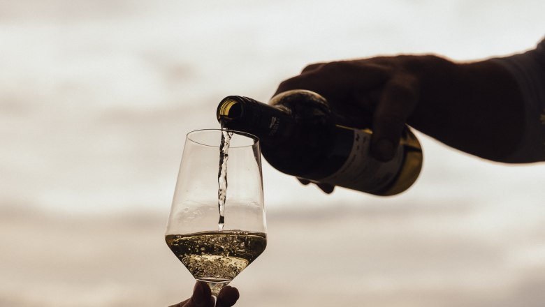 Pouring wine, © Weinviertel Tourismus / Sophie Menegaldo Wine is poured into a glass outdoors, with a landscape in the background.