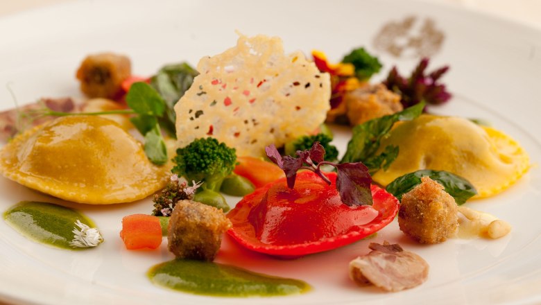 Culinary delights, © Fally An artfully prepared gourmet dish with ravioli, vegetables and herbs on a white plate.