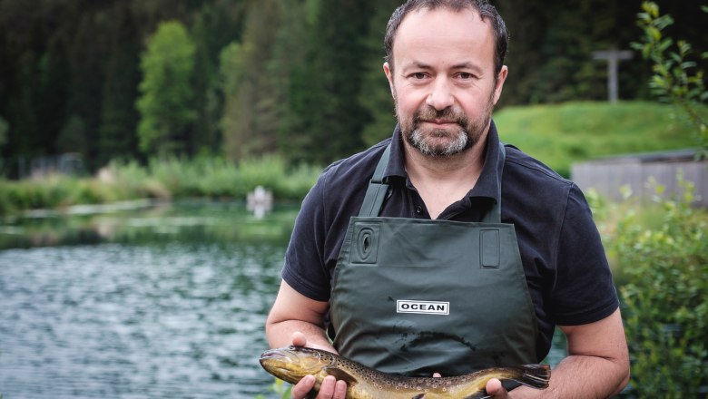 Martin Zöchling from Türnitz, © Rudy Dellinger A man in a green apron holds a fish in front of a pond.