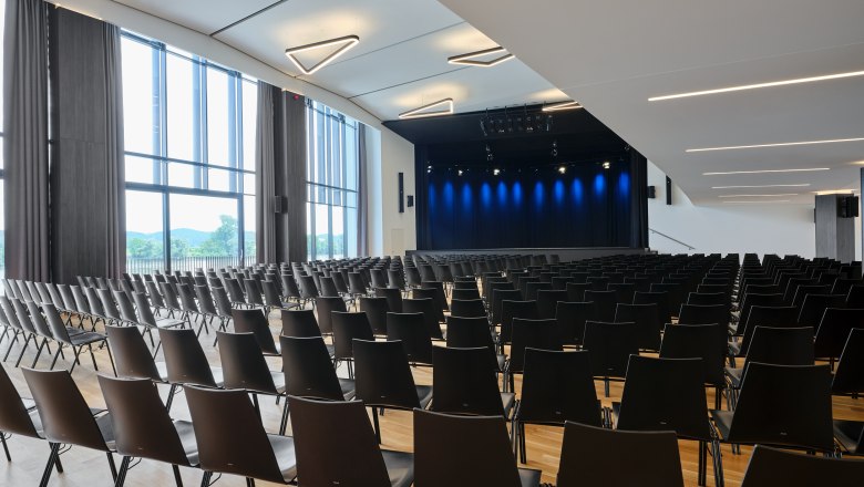 Stadthalle Ybbs stage, © Johann Perger Interior view of a modern event hall with empty black chairs and a stage with blue lighting.