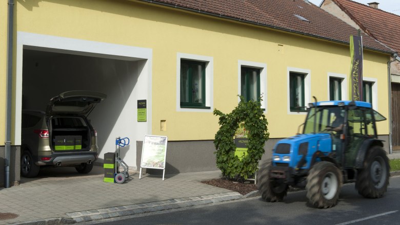 Wine delivery, © Weingut Holzmann Yellow building with open garage, car and tractor in front of it.