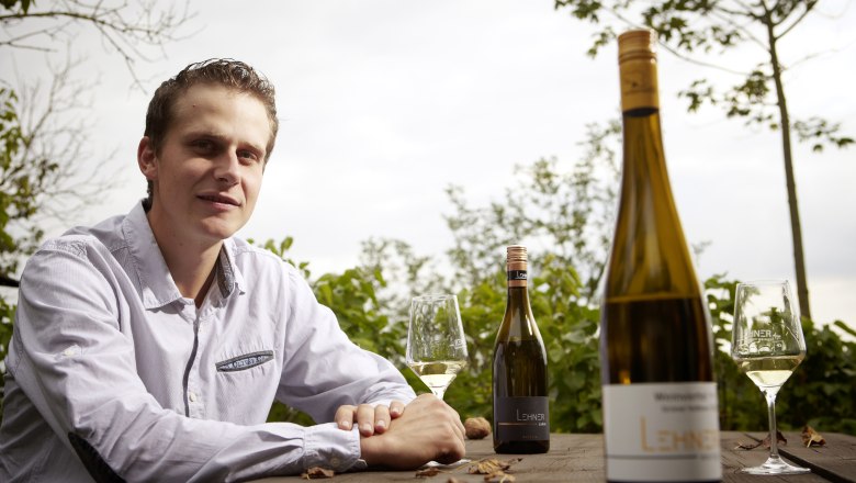 Lukas Lehner, © Lehner A man sits at a wooden table outside with bottles of wine and glasses.