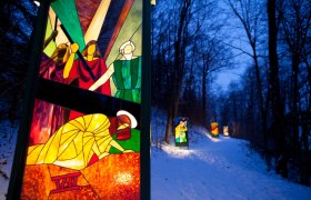 St. Ulrich's Church and the Glass Way of the Cross, © Thermengemeinden The illuminated stations of the Stations of the Cross made of colored glass on a winter evening with snow