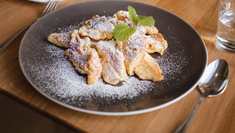 Rahmschmarrn with roasted apricots, © Niederösterreich Werbung/Daniela Führer A plate of Rahmschmarrn, sprinkled with powdered sugar and garnished with mint leaves, on a wooden table.