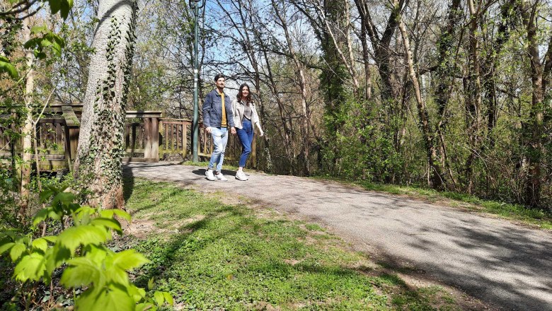 3 footbridges, Kleine Au, Fischamend, © Donau Niederösterreich, Neubauer A couple walks along a path in a wooded park.