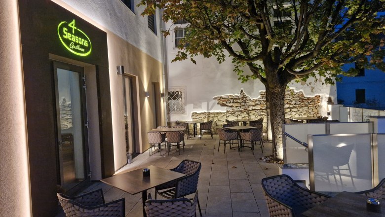 TD Terrace 4 Season, © Hendler Outdoor terrace of a restaurant with tables and chairs, illuminated at dusk, tree in the background.