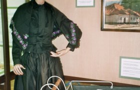 Traditional costume doll, © Adolf Haider A mannequin in traditional clothing next to an old baby carriage in a showroom.