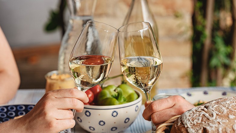 Wine enjoyment, © Michael Reidinger Two people toast with glasses of white wine, fruit and bread in the background.