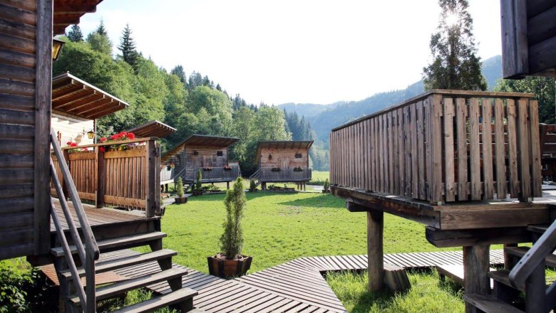 Sulzbichl adventure village, © weinfranz.at Wooden huts in a green valley with forest in the background.