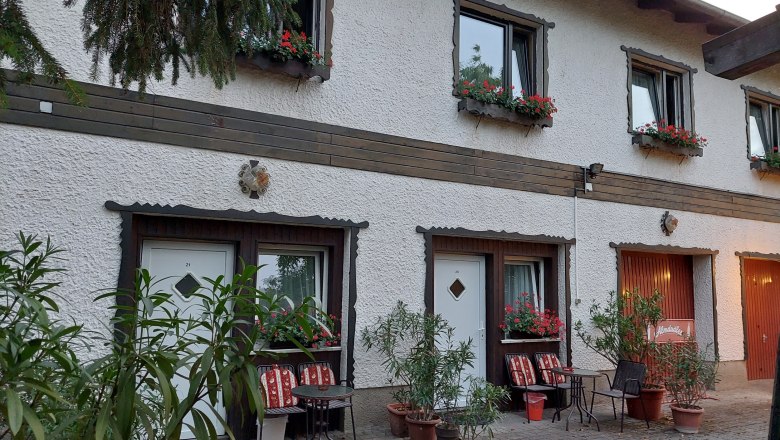 TDR-Welserhof-outside, © Nora Bartfai Exterior view of a two-story building with white walls, flower boxes and seating in front of the doors.