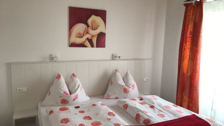 Bedroom in Loft 2, © Konstantin Hübner Bedroom with double bed, floral bedding, red picture and curtains.