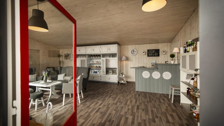 Info & pleasure filling station Hochneukirchen, © Marktgemeinde Hochneukirchen / Stefan Knittel Interior view of a cozy café with wooden floor, white furniture and decorative elements.