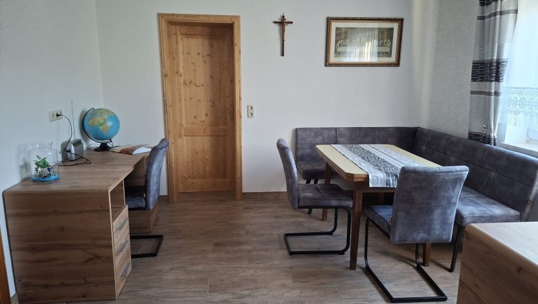 Dining area, © Ferienwohnung Penz Stolzenthal, Fotograf Hermine Penz Dining room with wooden table, gray chairs, a desk with a globe and a cross on the wall.
