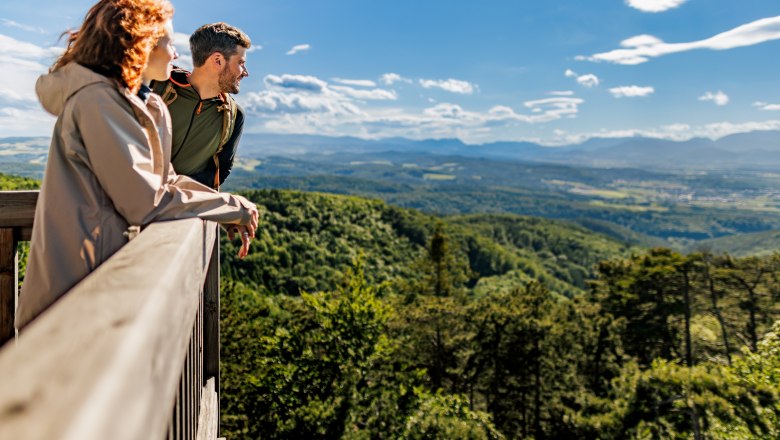 View over the hills of the Bucklige Welt, © Wiener Alpen, Fülöp, Kremsl Two people stand on the viewing platform and look out over a wooded, hilly landscape.