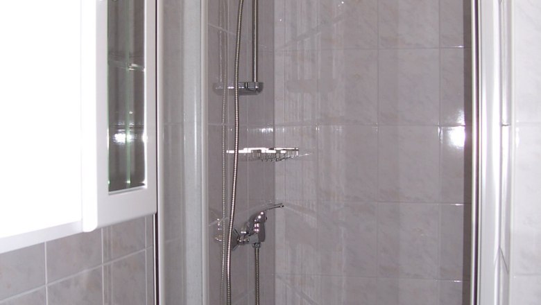 Shower, © Reep A modern shower cubicle with glass doors and chrome shower head in a tiled bathroom.
