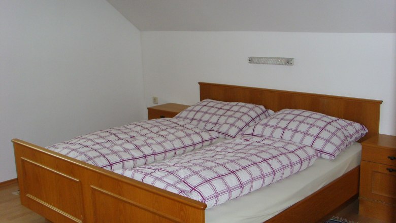 Private room Eder, © Eder Bedroom with wooden bed and plaid bedding.