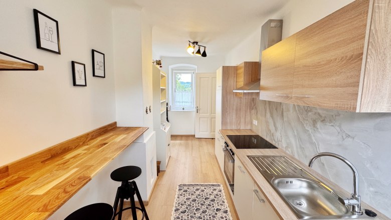 Kitchen, © Christoph Menhofer Modern kitchen with wooden worktops, white cupboards and bar stools. Minimalist pictures hang on the wall.